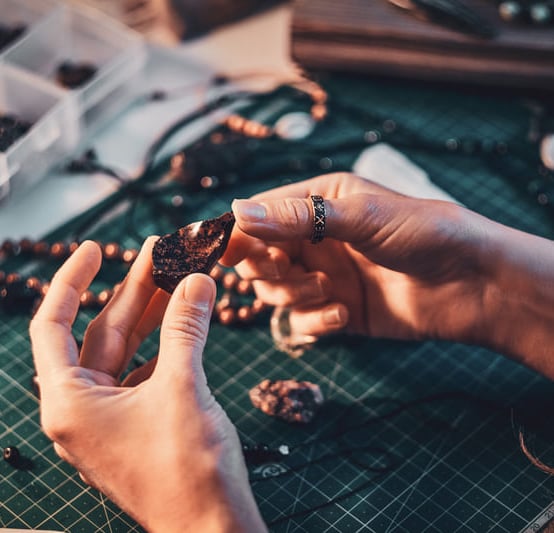 Artesano joyero inspeccionando una gema de obsidiana oscura sobre una mesa de trabajo con cuentas.