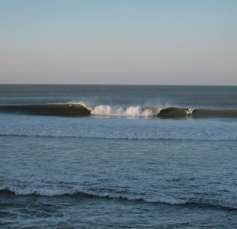 A large A frame peak, with a surfer taking off on the wave peeling to his left.