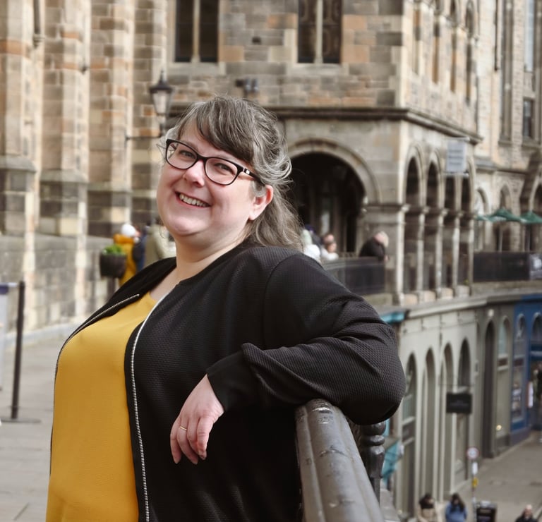Laura is leaning against a railing and smiling at the camera