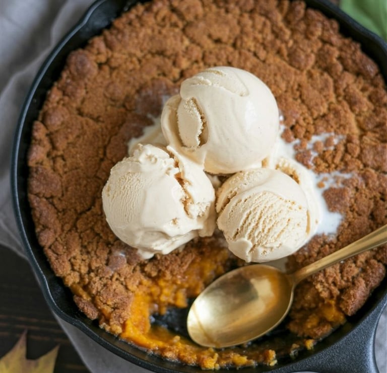 Warm pumpkin crisp topped with scoops of vanilla ice cream in a black skillet.