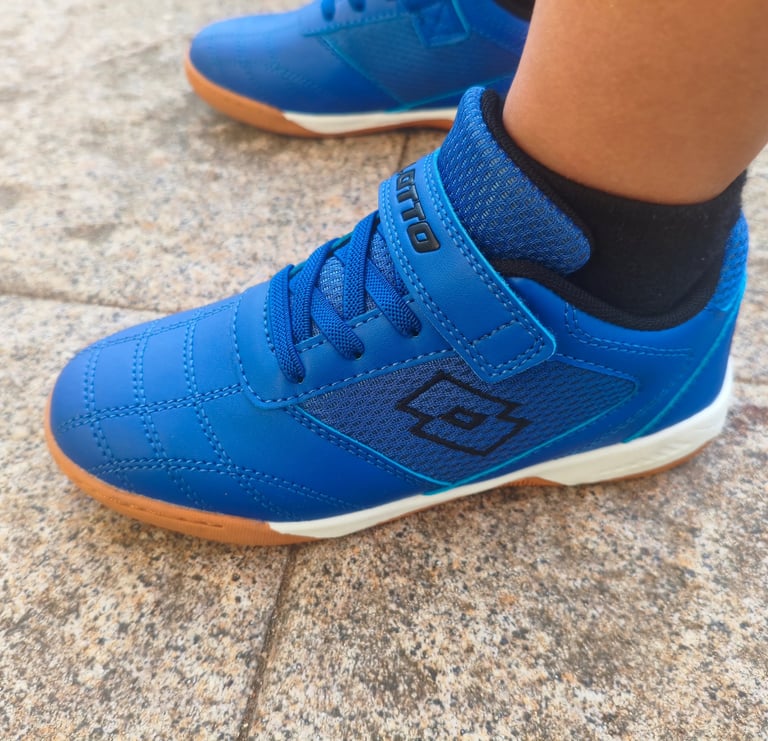 Criança a usar sapatilha infantil Lotto azul com velcro e sola laranja num chão de calçada