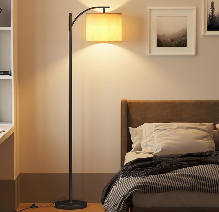 Modern black arc floor lamp with a linen drum shade illuminating a cozy bedroom bedside.