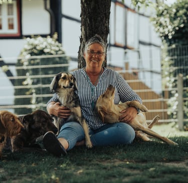 Marion sitzt an einen Baum gelehnt, zusammen mit ihren Hunden.