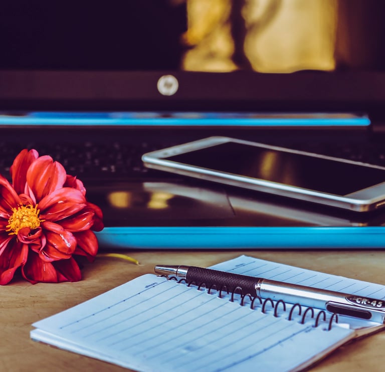 Téléphone portable posé sur le clavier d'un ordinateur avec un carnet, stylo et une fleur rouge posés à côté
