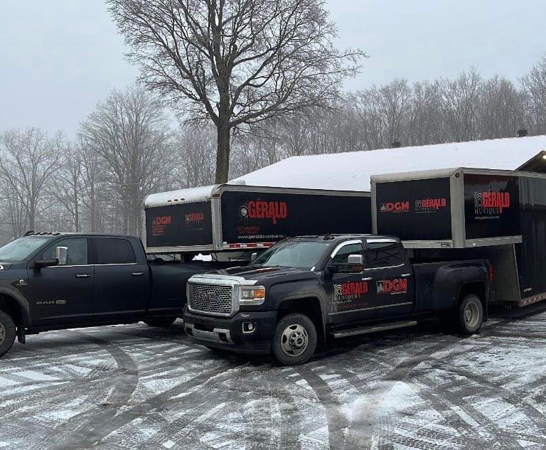 Black heavy-duty pickup trucks towing Gerald Musique equipment trailers in a snowy parking lot.