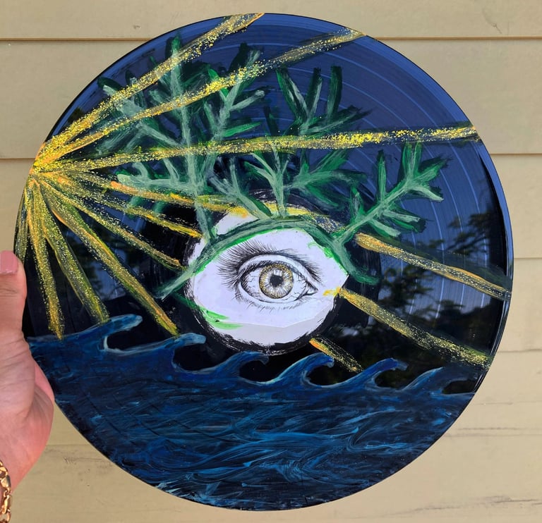 Hand-painted vinyl record art featuring an eye, green leaves, ocean waves, and gold glitter sun rays.