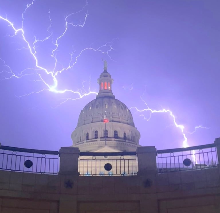 A photo of the Texas capitol dome with a thunderbolt crossing the sky during a spring thunderstorm.