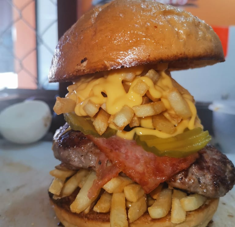 Hamburguesa de carne gourmet con papas fritas crujientes, salsa de queso fundido, pepinillos y jamón