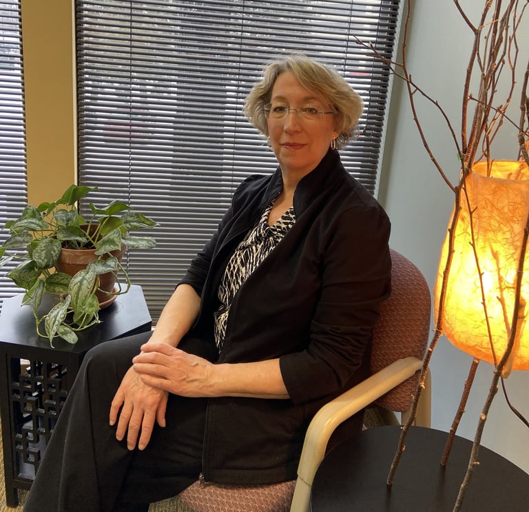 Dr. Jennifer Naas sitting in front of a window with closed blinds, creating a calm and focused setting.