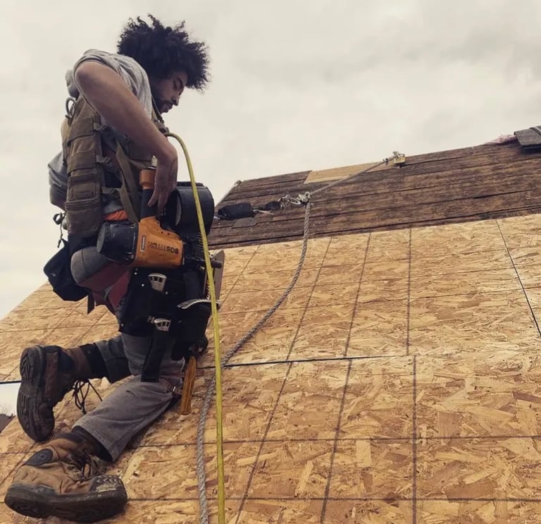 Professional roofer using a pneumatic nail gun to install plywood sheathing on a residential roof.