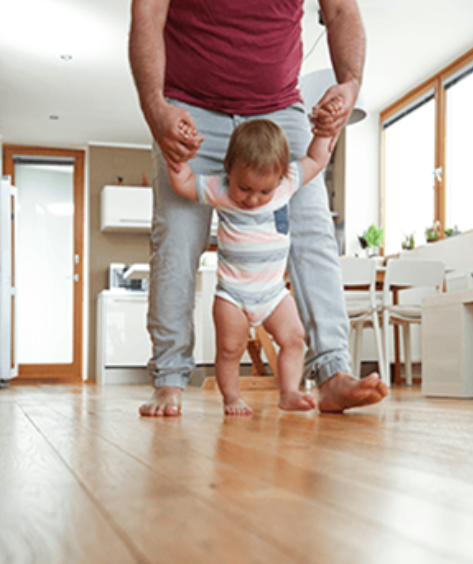 a man holding a baby's hand while standing on a hardwood floor