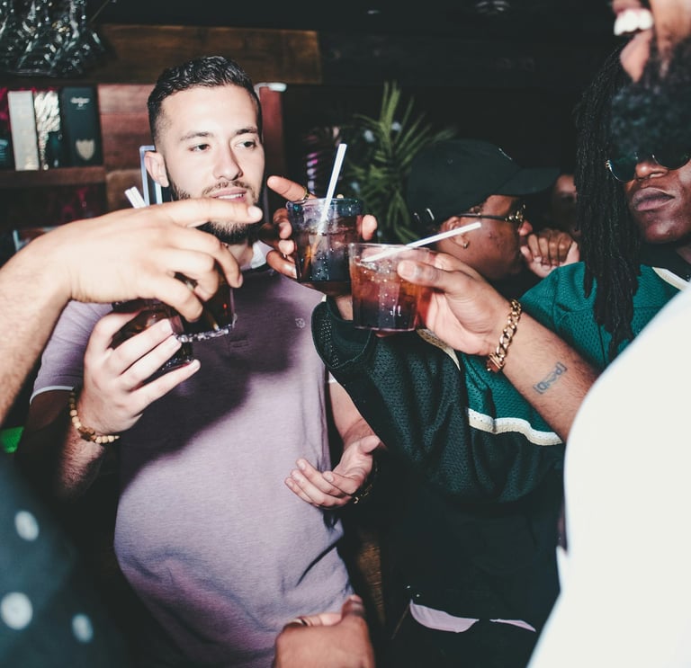 Friends clinking cocktails and celebrating at a dimly lit nightclub party.
