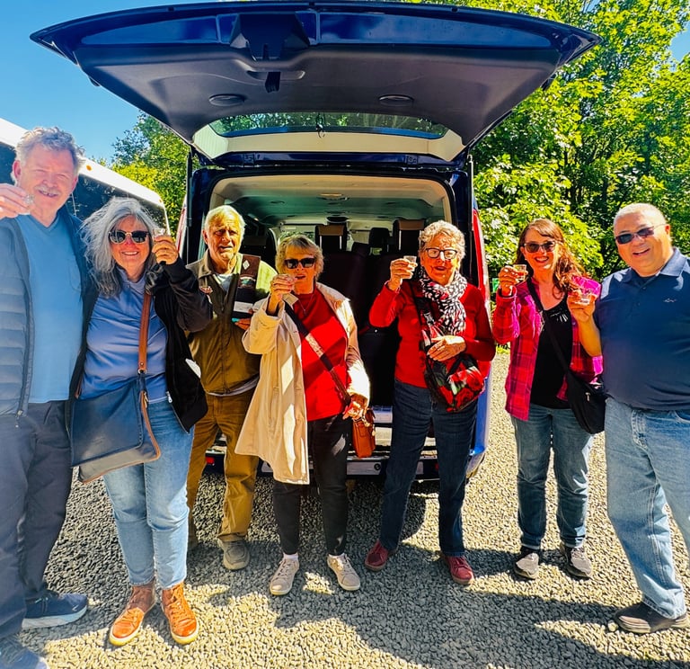 a group of people standing around a van smiling at the camera with drinks in their hands