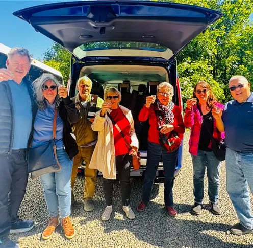 a group of people standing around a van smiling at the camera with drinks in their hands