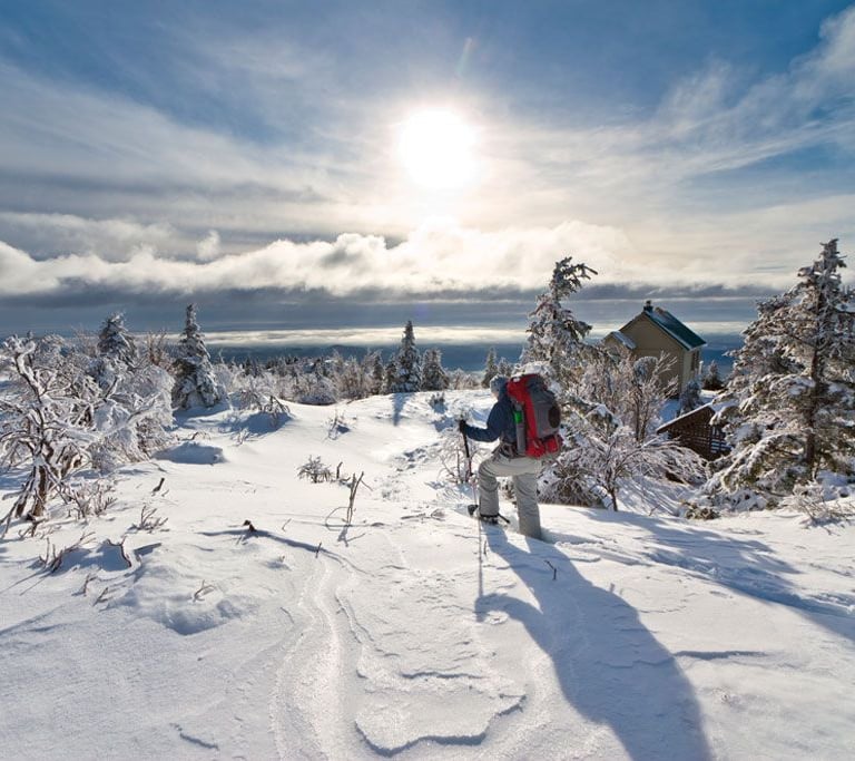 Randonneur en raquettes explorant les paysages enneigés des Monts-Valin à la SEPAQ, profitant de la beauté naturelle et de l'