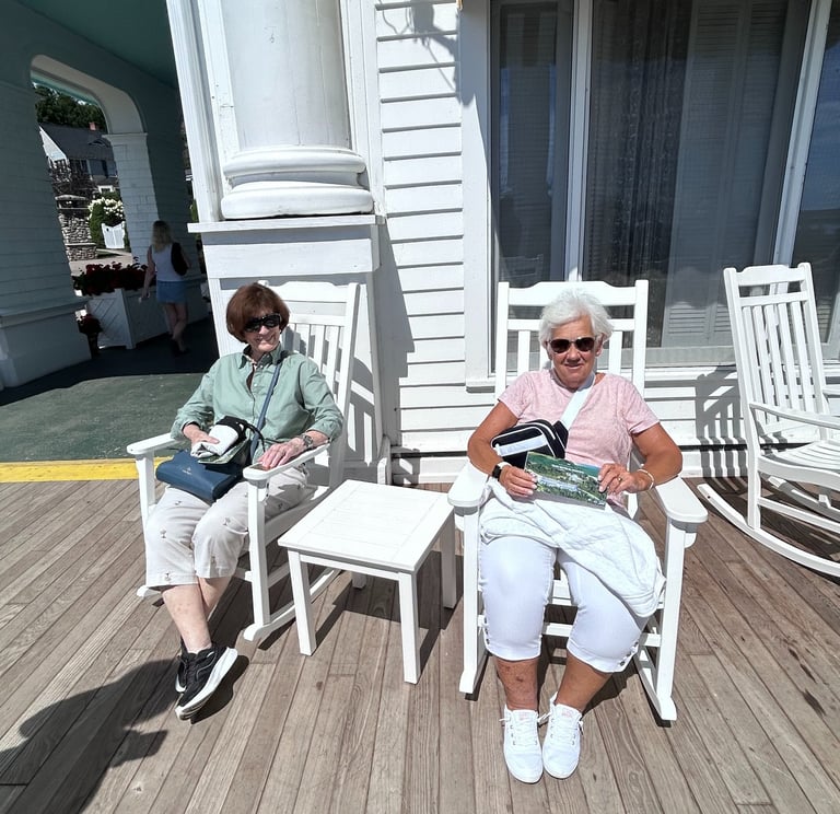 A picture of 2 women sitting in rocking chairs on the porch of the hotel.