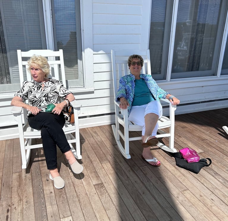 A picture of 2 women sitting in rocking chairs on the porch of the hotel.