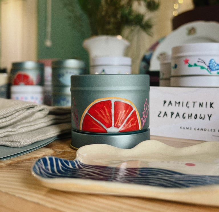 Hand-painted citrus scented candle in a grey metal tin on a wooden table with ceramic dish.