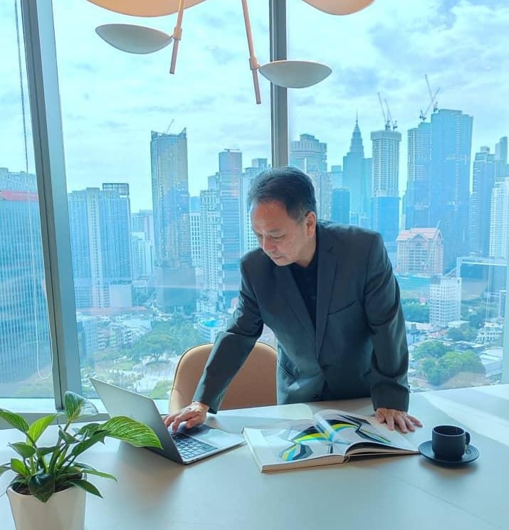 Professional businessman in a suit working on a laptop in a high-rise office with a city skyline view.