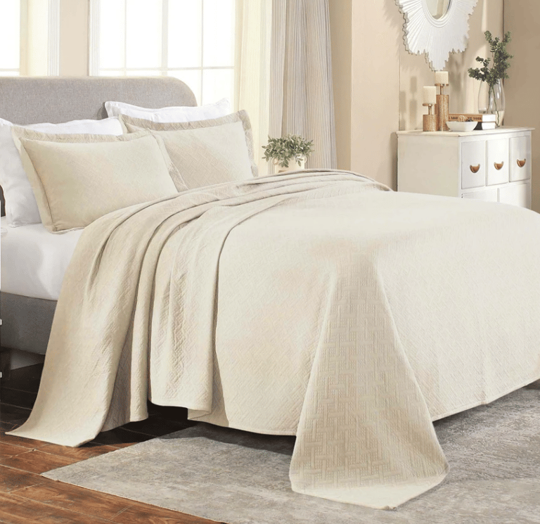 Elegant beige quilted coverlet set on a modern bed with matching pillow shams in a neutral bedroom.
