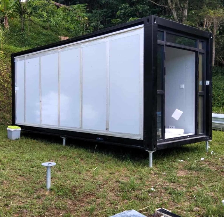 Maison conteneur noire préfabriquée sur pieux vissés dans un champ.