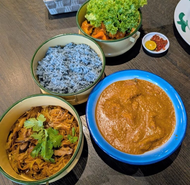Peranakan Nyonya cuisine featuring blue pea rice, chicken curry, and stir-fried vegetables in tiffin carriers.