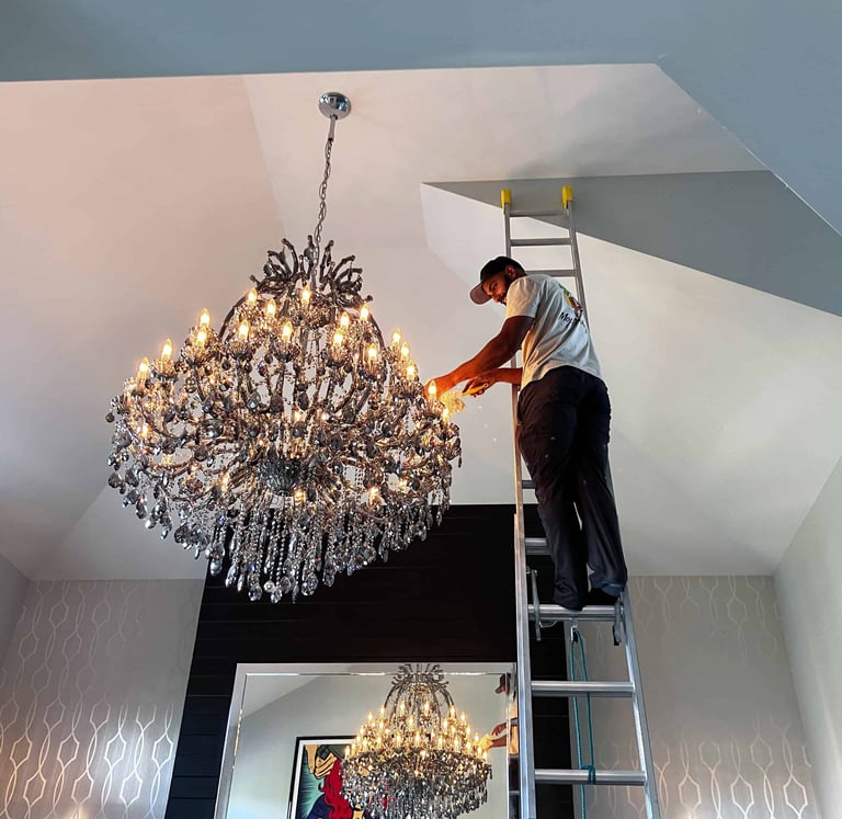 Mop Monkey technician dusting crystal chandelier from ladder in Calgary
