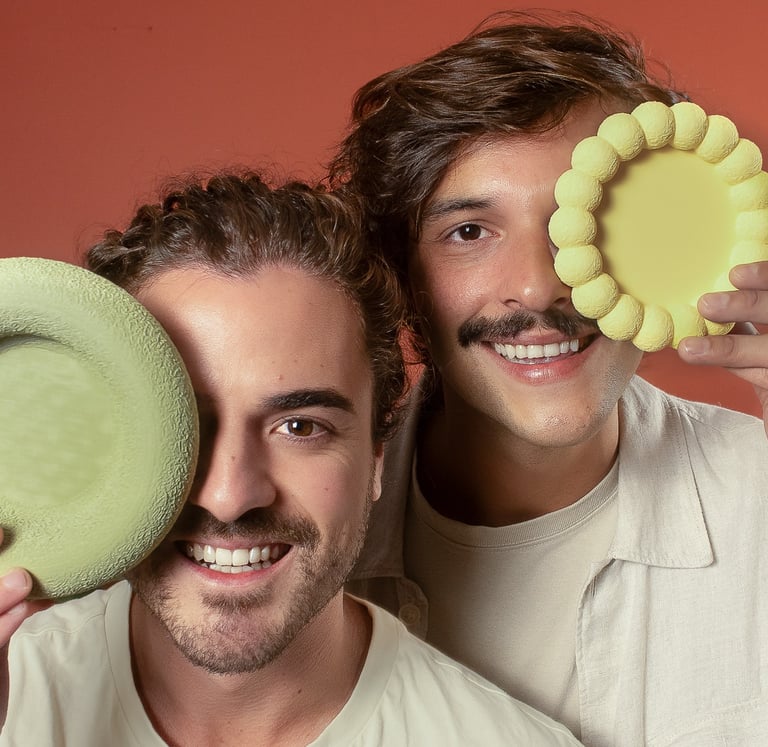 Daniel e Filipe, fundadores da Tidu Home, segurando objetos decoratios em 3D.
