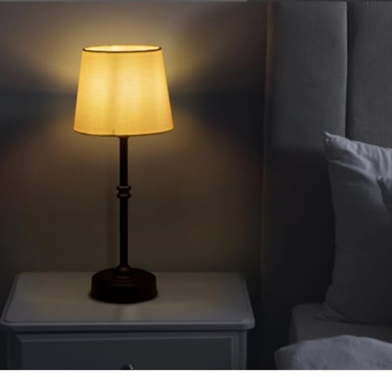 Elegant bronze bedside table lamp with a warm glowing fabric shade on a white nightstand.