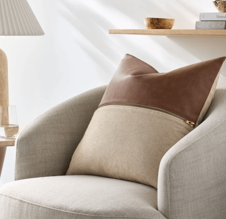 Modern faux leather and beige linen decorative throw pillow on a contemporary upholstered armchair.