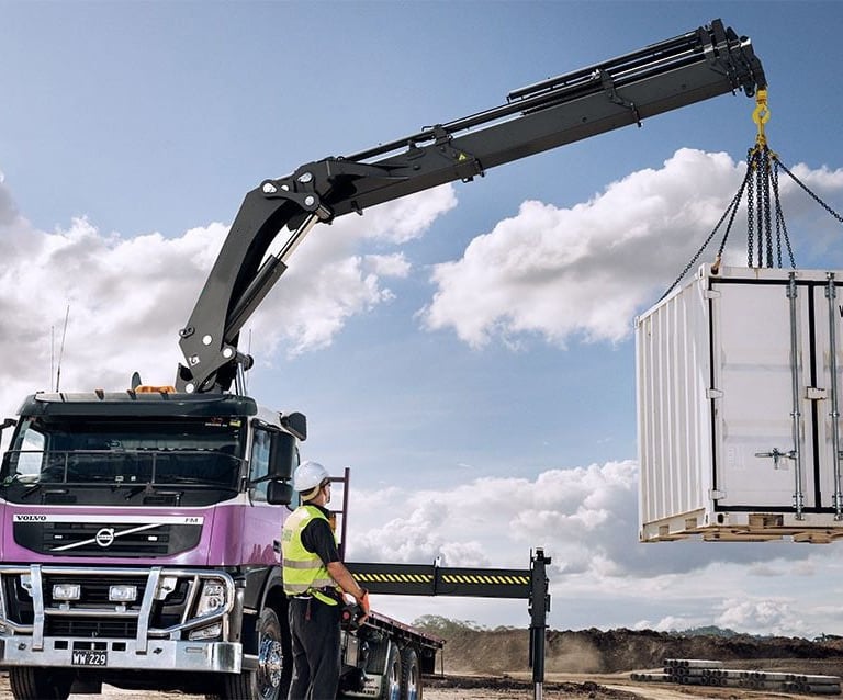 A knuckle boom crane with RC lifting a container onto a truck.