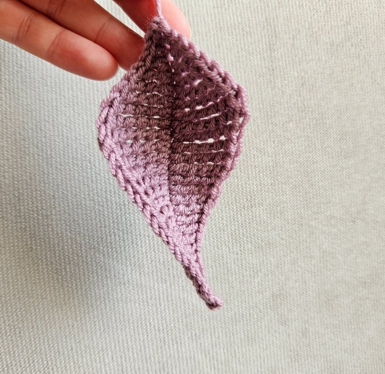 Handmade mauve crochet leaf pattern held against a neutral fabric background for DIY crafts.