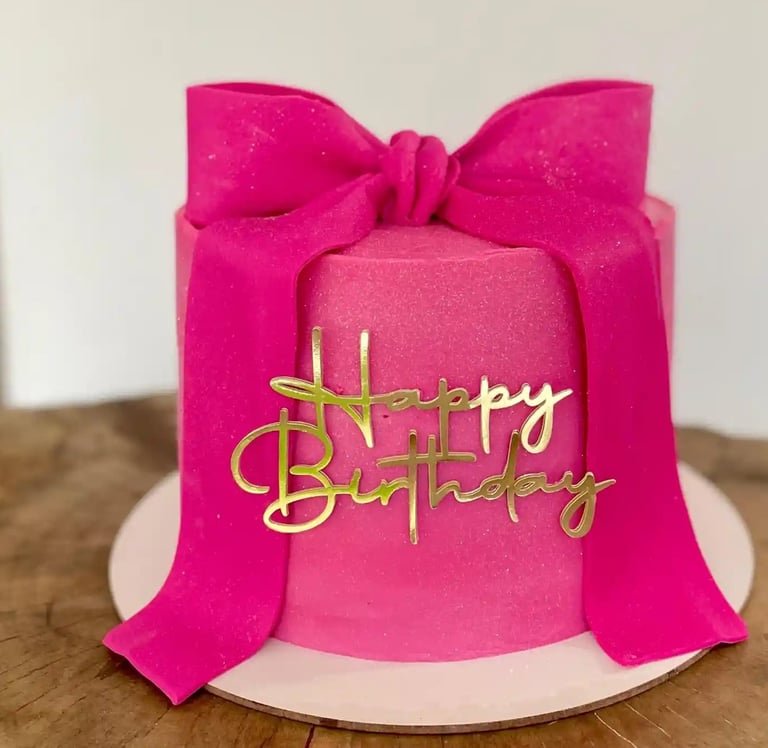 Bolo de aniversário decorado em rosa com fita e detalhes dourados. Ideal para festas e comemorações