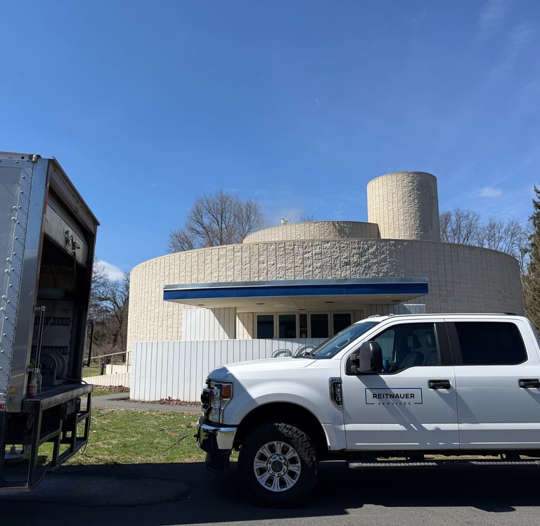 Reitnauer Services white Ford pickup truck parked next to a service box truck near a circular stone building.