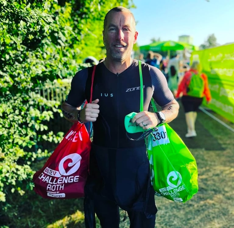 A male triathlete carrying red and green transition bags at the DATEV Challenge Roth triathlon event.