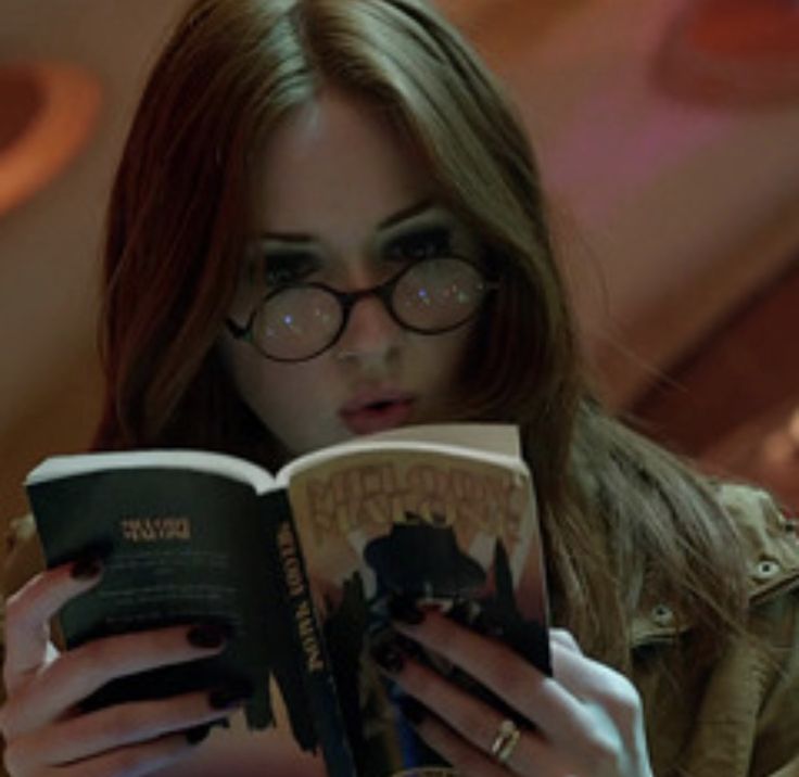 a woman in glasses and a jacket is reading a book