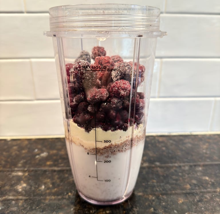 Protein smoothie ingredients layered in a blender cup with berries and almond milk.