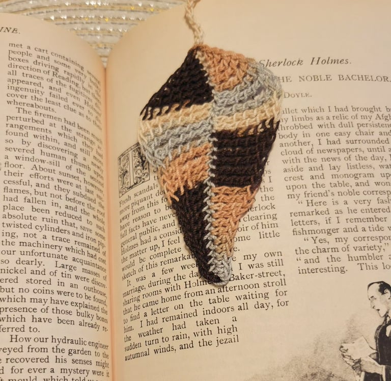 Handmade brown and tan crochet leaf bookmark resting on pages of a Sherlock Holmes book.
