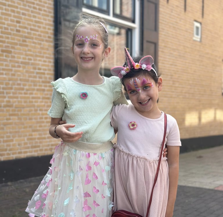 Meisje met roze en paarse eenhoorn-schmink en een bloemenhaarband.