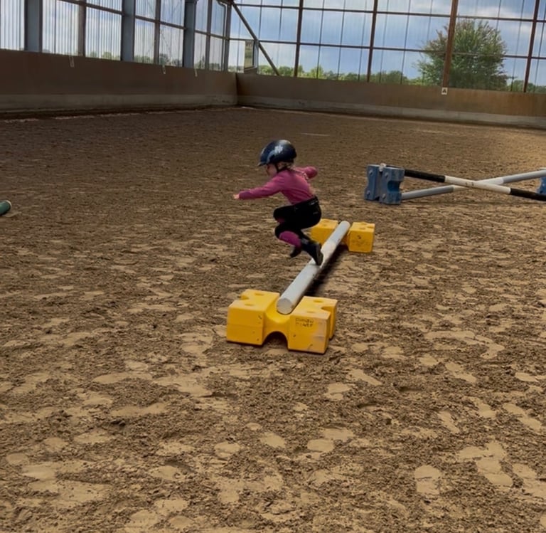 Young child in a riding helmet jumping over a hurdle in an indoor horse riding arena. Ponytante