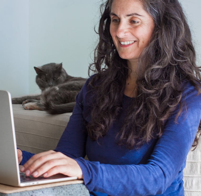 Porträt von Juliette Maggu am Laptop mit einer Katze im Hintergrund