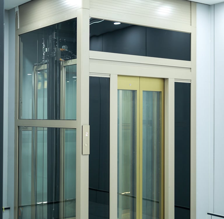 Modern residential glass elevator with gold trim and a beige metal frame installed in a luxury home.