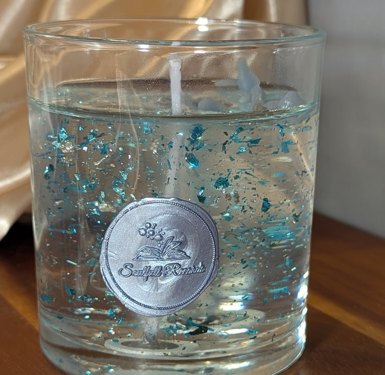 Clear gel candle in a glass jar featuring decorative blue glitter flakes and a silver wax seal logo.