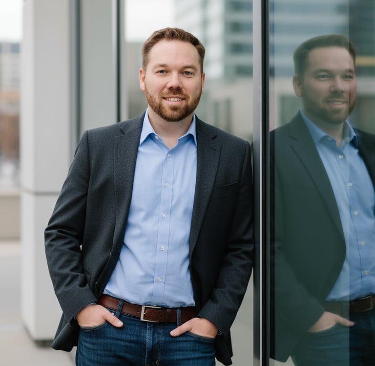 Man in blazer and jeans leaning against glass wall with city buildings in background.