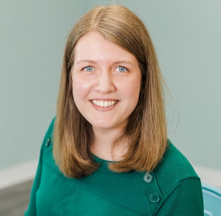 a woman with blue eyes and a green sweater.  dark blond hair, blue eyes.  She's smiling