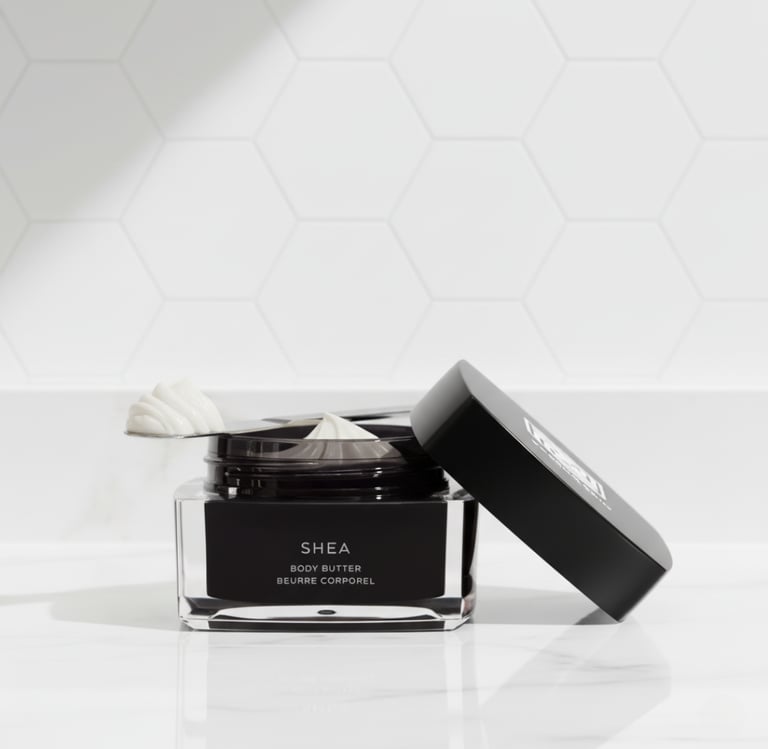 Jar of shea body butter moisturizer on a marble counter with white honeycomb tile background.