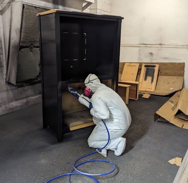 woman in protective suit and respirator spray painting a wardrobe