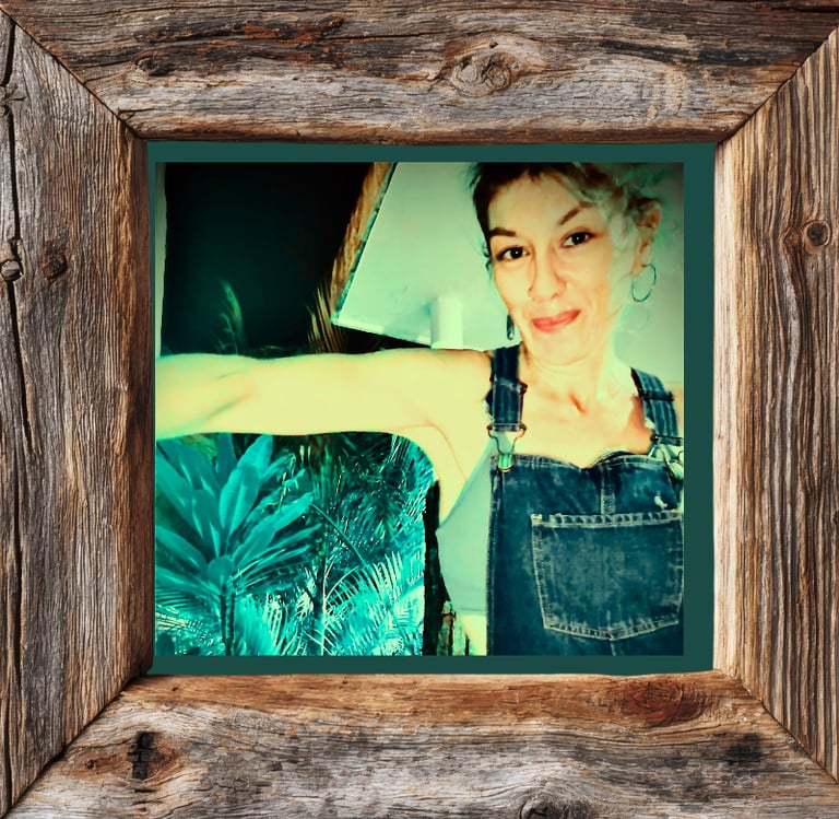 Smiling woman in denim overalls framed by rustic reclaimed wood with tropical plants in background.