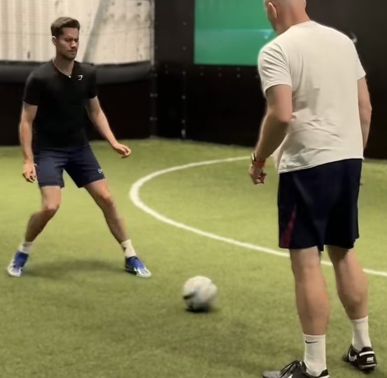 Two people taking part in a football activity on an indoor artificial pitch.