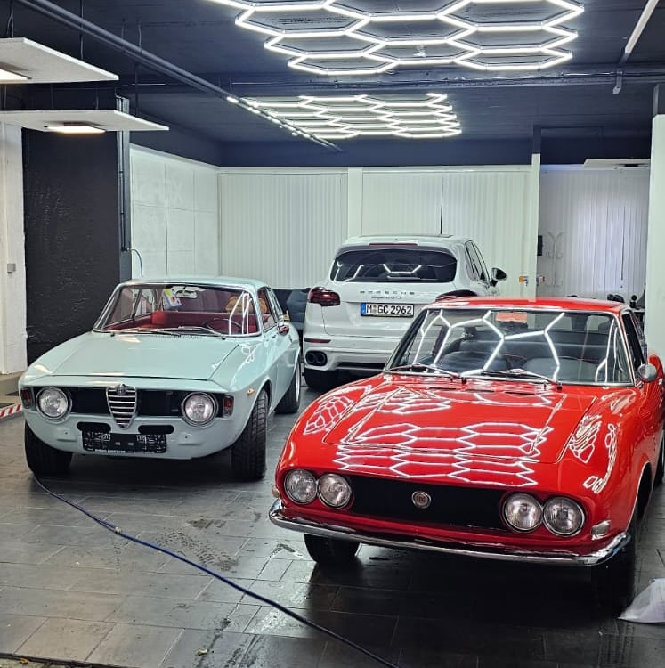 Zwei klassische Sportwagen (rot und weiß) in einer Werkstatt oder Ausstellungshalle.